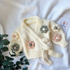 a knitted sweater with flowers on it next to a potted plant and cardigan