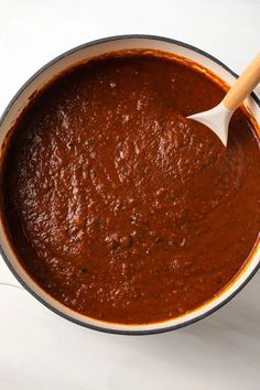 a pot filled with red sauce on top of a white counter next to a wooden spoon