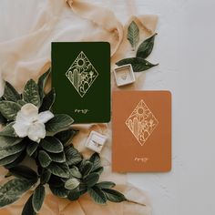 two notebooks and some flowers on top of a white table with green wrapping paper