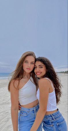 two young women standing next to each other on a beach