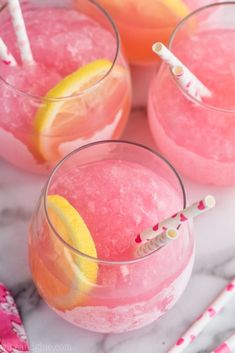 three glasses filled with pink lemonade and two straws next to each other on a marble surface