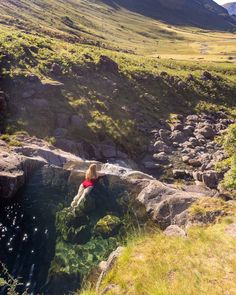 a person sitting on top of a rock in the middle of a mountain stream with mountains in the background