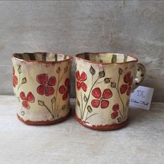 two red flowered cups sitting next to each other on top of a white table