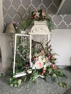 an arrangement of flowers and greenery is displayed on a shelf in the corner of a room