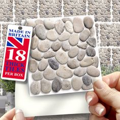 a hand holding a small white box with rocks in it and a british flag tag hanging from the front