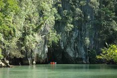 two boats are in the water near some rocks and trees on either side of them