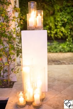 candles are lit in front of a tall pillar with glass vases on the side