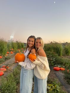 two women standing in a field holding pumpkins