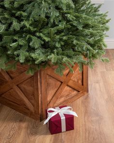 a christmas tree with a red present box under it on the floor next to a wooden planter