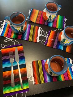 three cups of hot chocolate sit on colorful placemats with forks and spoons