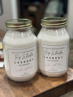 two glass jars sitting on top of a wooden table next to each other with labels on them