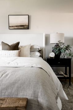 a bed with white linens and pillows in a bedroom next to a painting on the wall