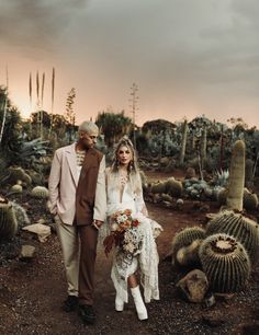 a bride and groom walking through the desert at sunset with cacti in the background