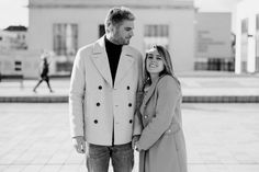 a man and woman standing next to each other in front of a building with people walking by