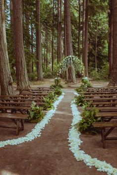 an outdoor wedding ceremony in the woods with white flowers and greenery on the aisle