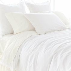 a bed with white sheets and pillows in a bedroom