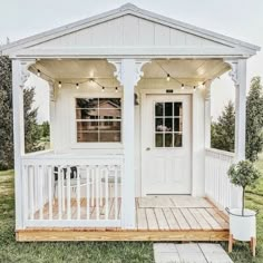 a small white house with porch and lights on the front door, sitting in grass