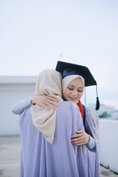 a woman in a graduation gown hugging another woman