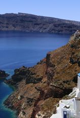 a white building on the side of a mountain with blue water in the middle and mountains behind it