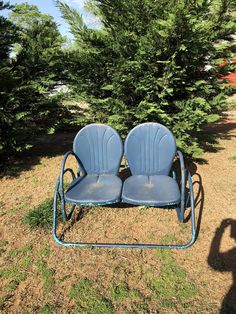 two blue chairs sitting in the grass near some trees