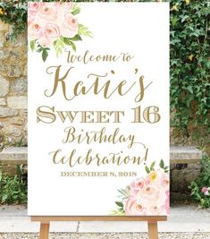 a welcome sign with pink flowers and greenery on it in front of a stone wall