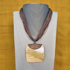 MOTHER OF PEARL SHELL WAXED LINEN CORD NECKLACE - BROWN DETAILS This boho mother of pearl necklace was designed using waxed linen cord and a huge Mother of pearl shell pendant. Handmade and imported from Thailand. 301635-BROWN Boho style necklace 18" long Mother of pearl shell pendant - 4" x 2 1/2" 5 strands of waxed linen cord Knotted waxed linen clasp Imported MATERIAL HIGHLIGHTS: Mother of Pearl: Calming, brings inner wisdom, mental clarity, intuition, sensitivity, imagination, adaptability, Luxury Artisan Hand Wrapped Necklaces, Luxury Handmade Beaded Necklaces With Mother Of Pearl, Luxury Beaded Mother Of Pearl Shell Necklace, Luxury Artisan Mother Of Pearl Necklaces, Luxury Artisan Necklace With Mother Of Pearl, Luxury Artisan Mother Of Pearl Necklace, Affordable Adjustable Mother Of Pearl Shell Necklace, Luxury Handmade Shell Pendant Necklace, Luxury Handmade Mother Of Pearl Shell Necklace