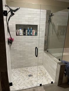 a walk in shower sitting next to a white tiled wall and floor with glass doors