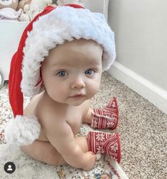 a baby wearing a santa hat and mittens sitting on the floor