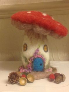 a mushroom house with a blue door and red roof sits on a shelf next to some pine cones