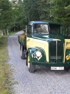 an old green and yellow truck parked on the side of a road next to trees