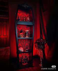 a tall black shelf with red wallpaper and flowers in the corner next to it