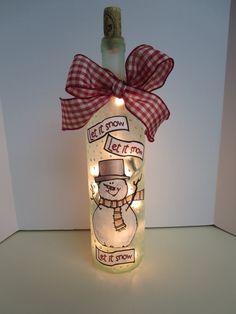 a lighted bottle with a snowman on it that says let it snow and is decorated with lights