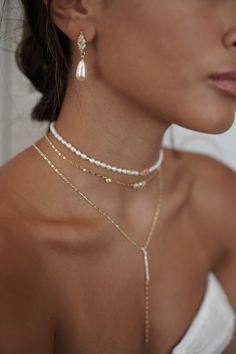 a woman wearing two necklaces with pearls on her neck and one is wearing a white dress