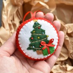 a hand holding a small felt ornament with a christmas tree decoration on it