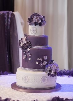 a purple and white wedding cake with flowers on the top is sitting on a table