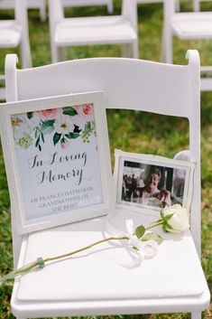 a white chair sitting in the grass next to a photo frame and flower on top of it