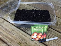 a container filled with dirt next to a packet of seeds and a pen on top of a wooden table