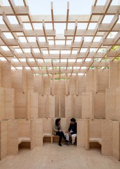 two people sitting in a room made out of plywood planks and wooden slats