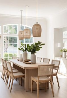 a dining room table and chairs with plants in vases on the top, near large windows