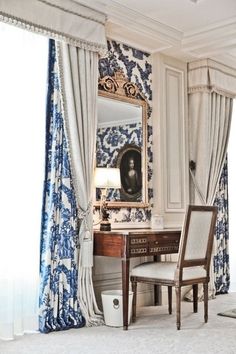 a desk with a mirror, chair and lamp in front of a curtained window