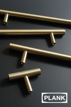 six brass tubes on a black surface with the word plank written in white above them