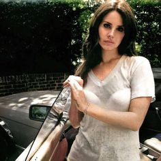 a woman standing next to a car with her hand on the door handle and looking at the camera