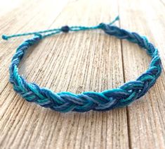 a close up of a bracelet on a wooden surface with blue and green yarn around it