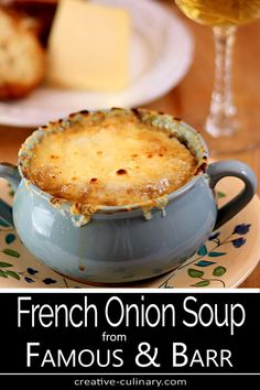 a french onion soup in a blue bowl on a plate next to a glass of wine