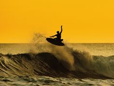 a person riding a surfboard on top of a wave in the ocean at sunset