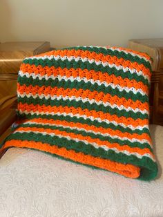 an orange and green crocheted blanket sitting on top of a bed