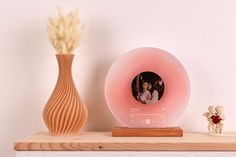 a pink alarm clock sitting on top of a wooden shelf next to a vase and teddy bear