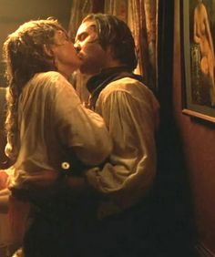 a man and woman kissing in front of a painting on the wall next to each other