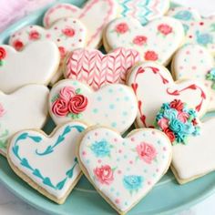 several decorated heart shaped cookies on a blue plate with pink and white flowers in the center