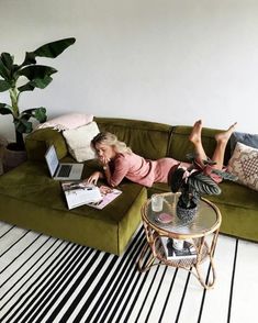 a woman laying on top of a green couch next to a table with a laptop